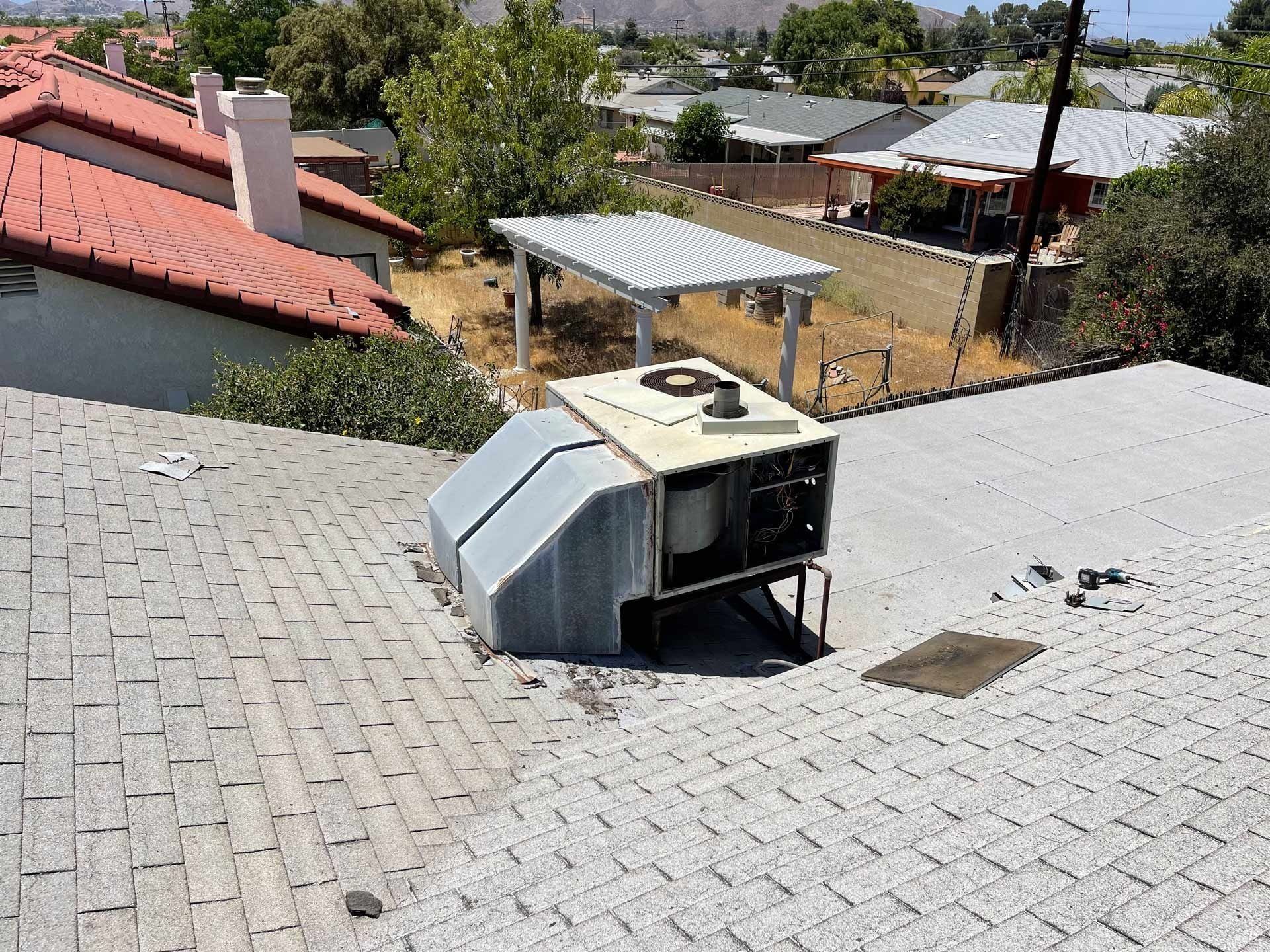 A large fan is sitting on top of a building next to pipes.