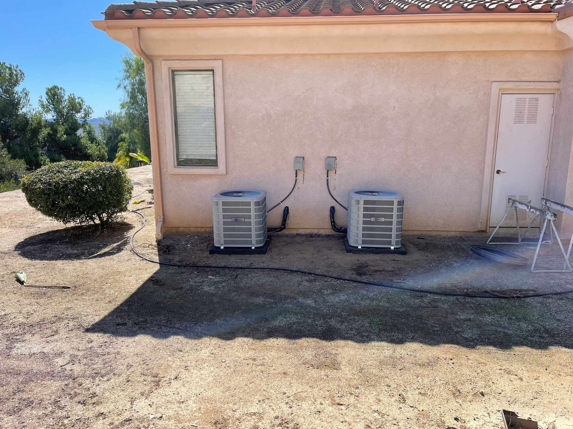 Two air conditioners are attached to the side of a house