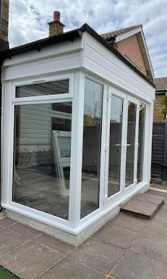 A white conservatory with a lot of windows and doors is in the backyard of a house.
