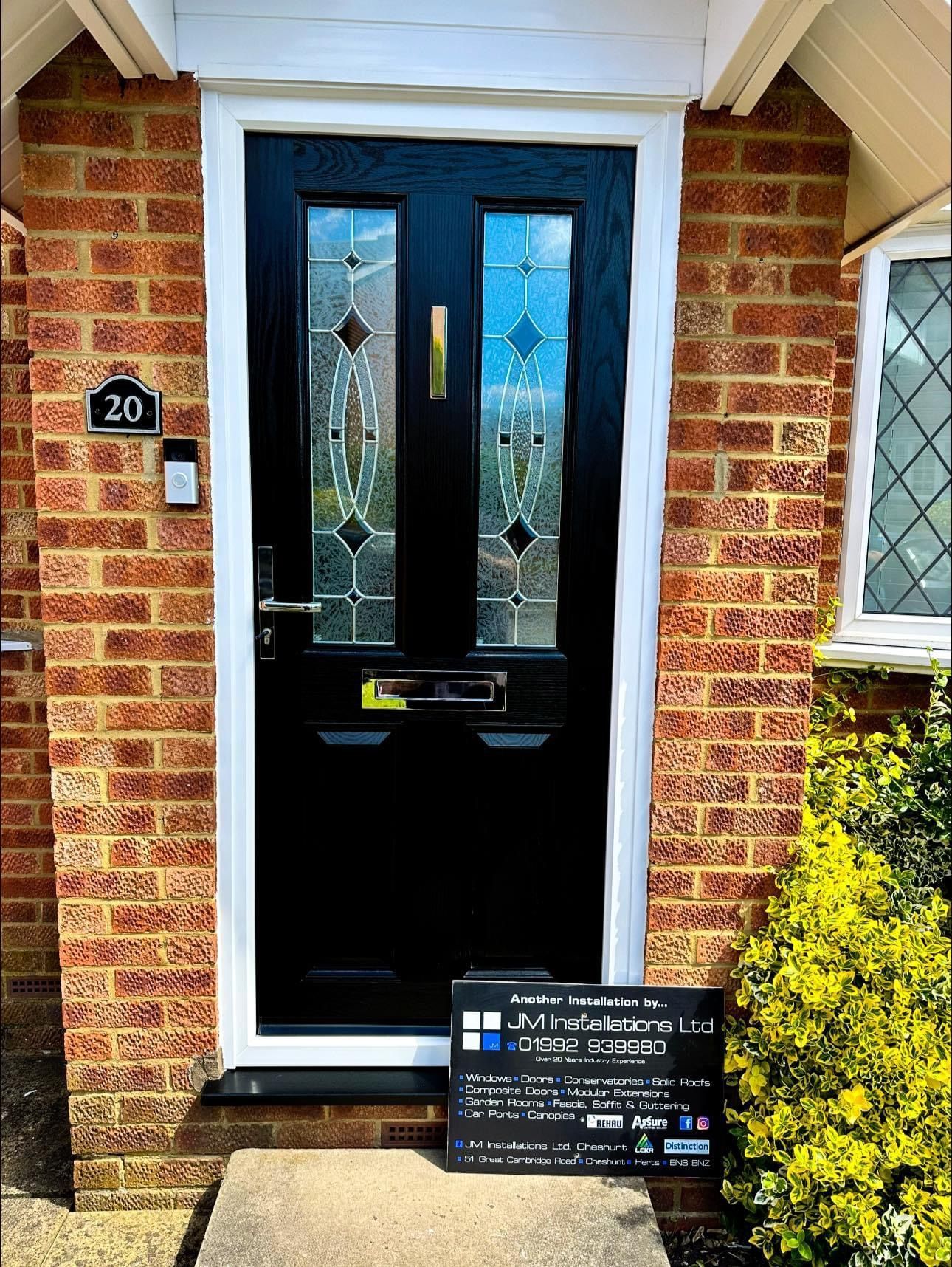 A black door with stained glass is on the front of a brick house.
