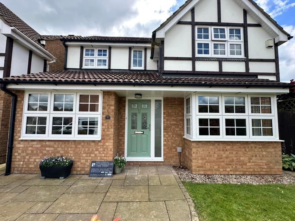 The front of a brick house with a green door and white windows.
