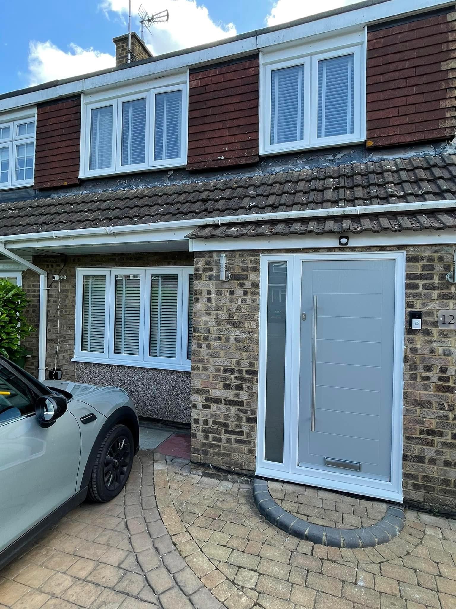 A white car is parked in front of a brick house.
