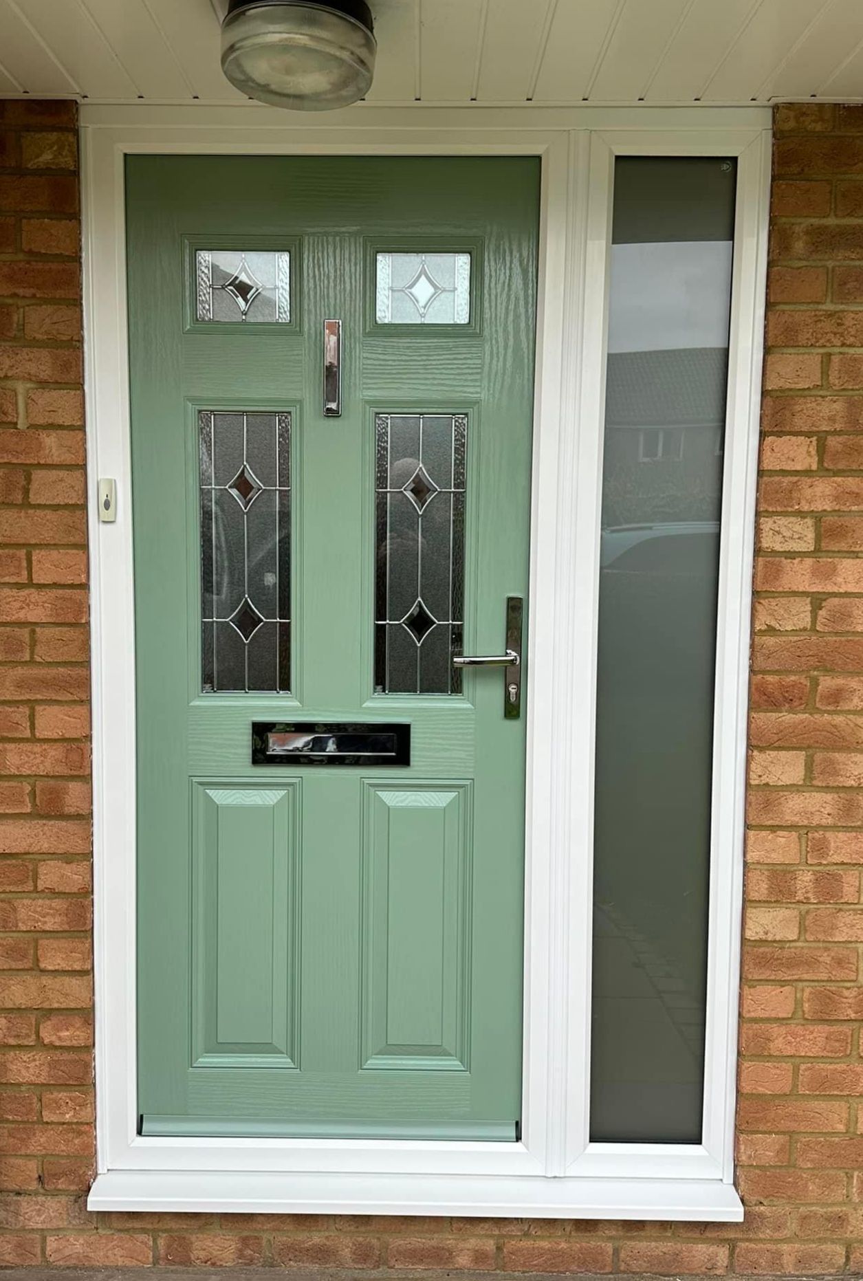 A green front door with a white frame is on a brick wall.