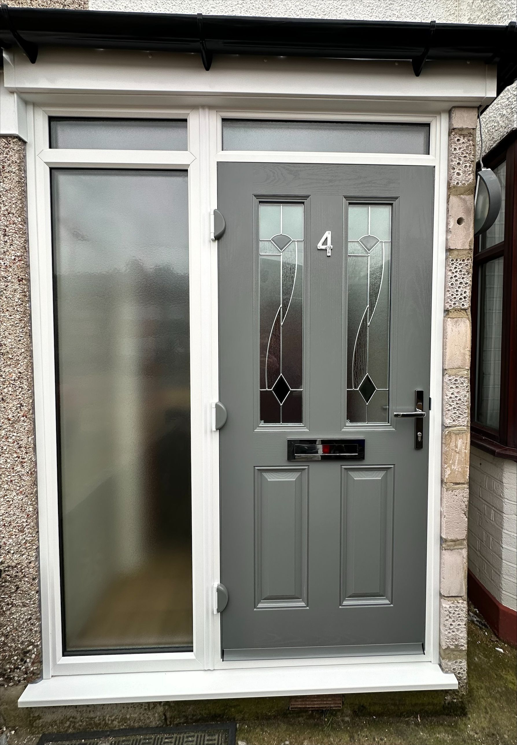 A gray front door with a white frame is sitting on the side of a house.