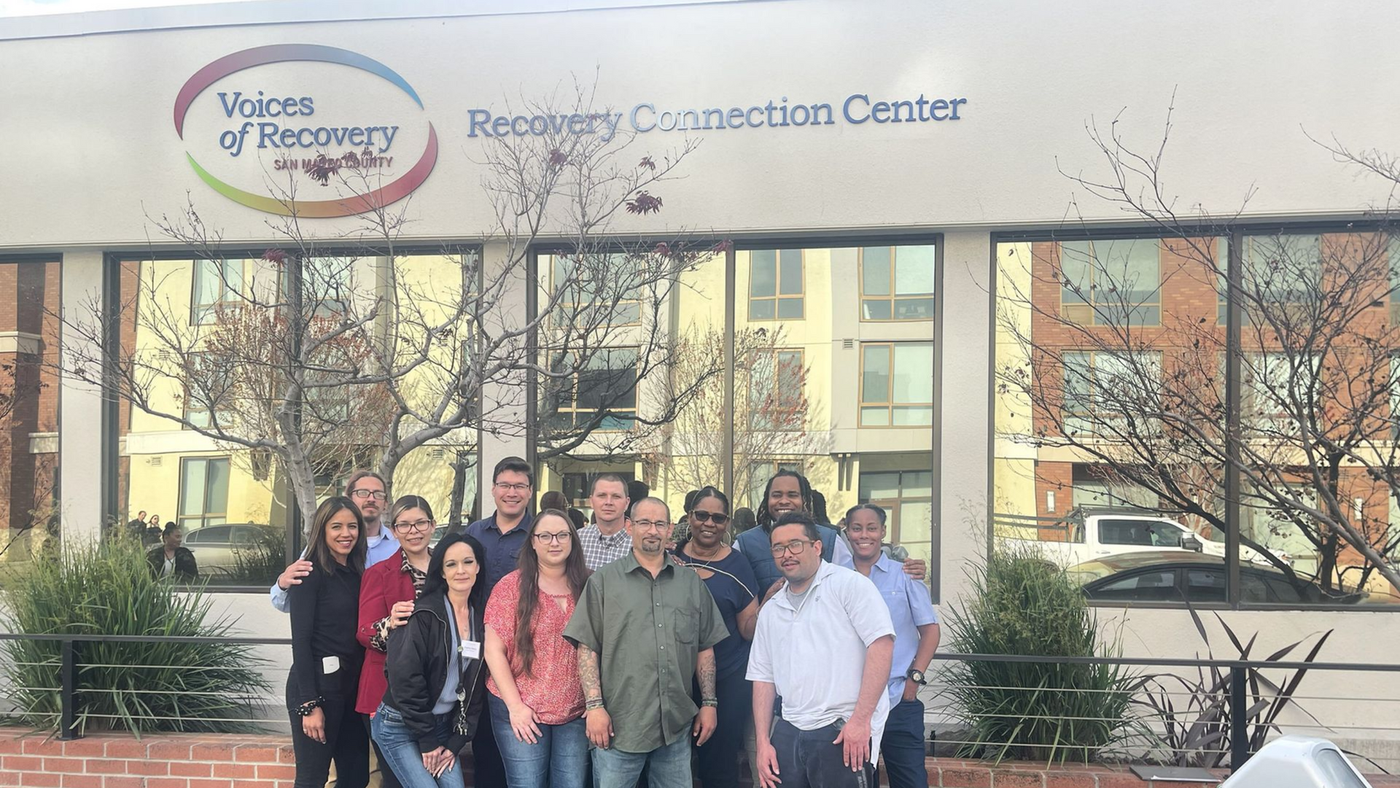 Group of people smiling in front of a building with
