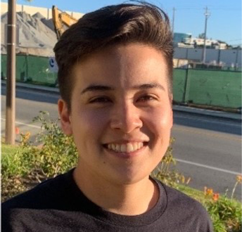 Smiling person with short brown hair, black shirt, outdoors on a sunny day.