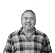 Man smiling in a plaid shirt, standing in front of a blurred background.