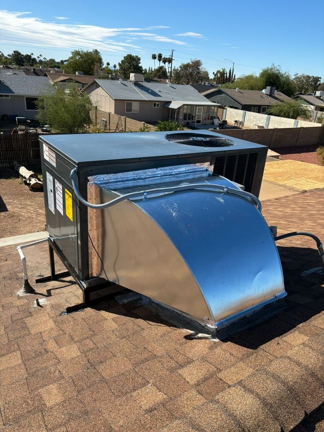 Portable metal air duct unit with a shiny curved vent on a rooftop, with houses in the background