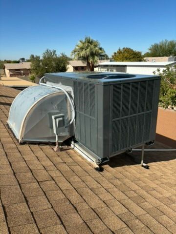 Roof-mounted HVAC units and ductwork on a tan shingle roof under a clear sky.