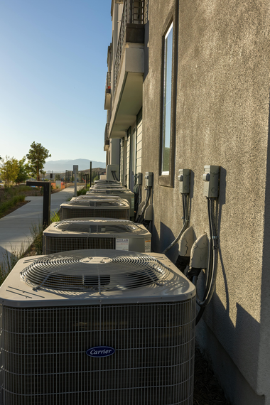Row of outdoor air conditioning units beside a beige building in bright sunlight
