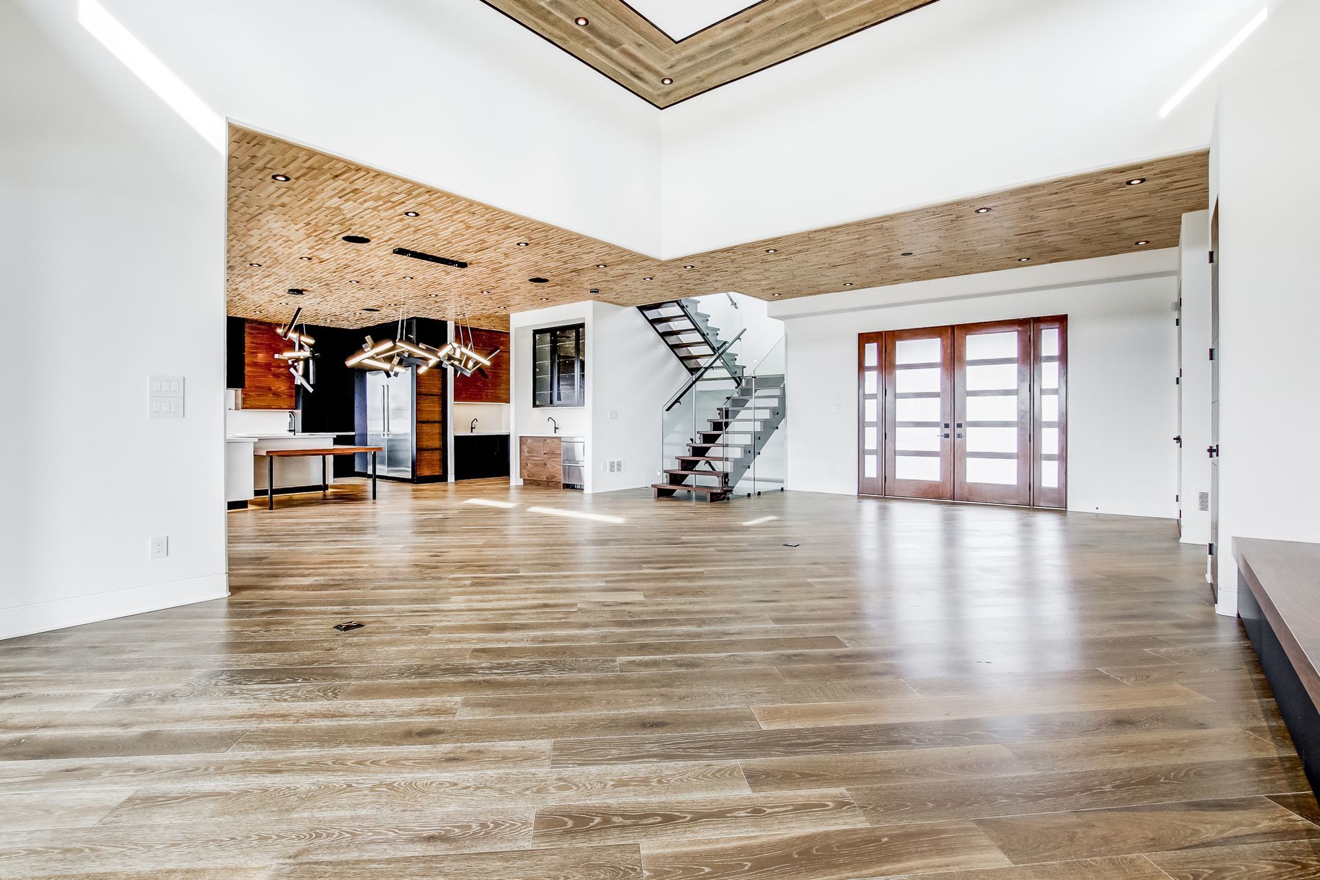 Spacious, empty room with wood floors, brick accent walls, and a modern staircase.