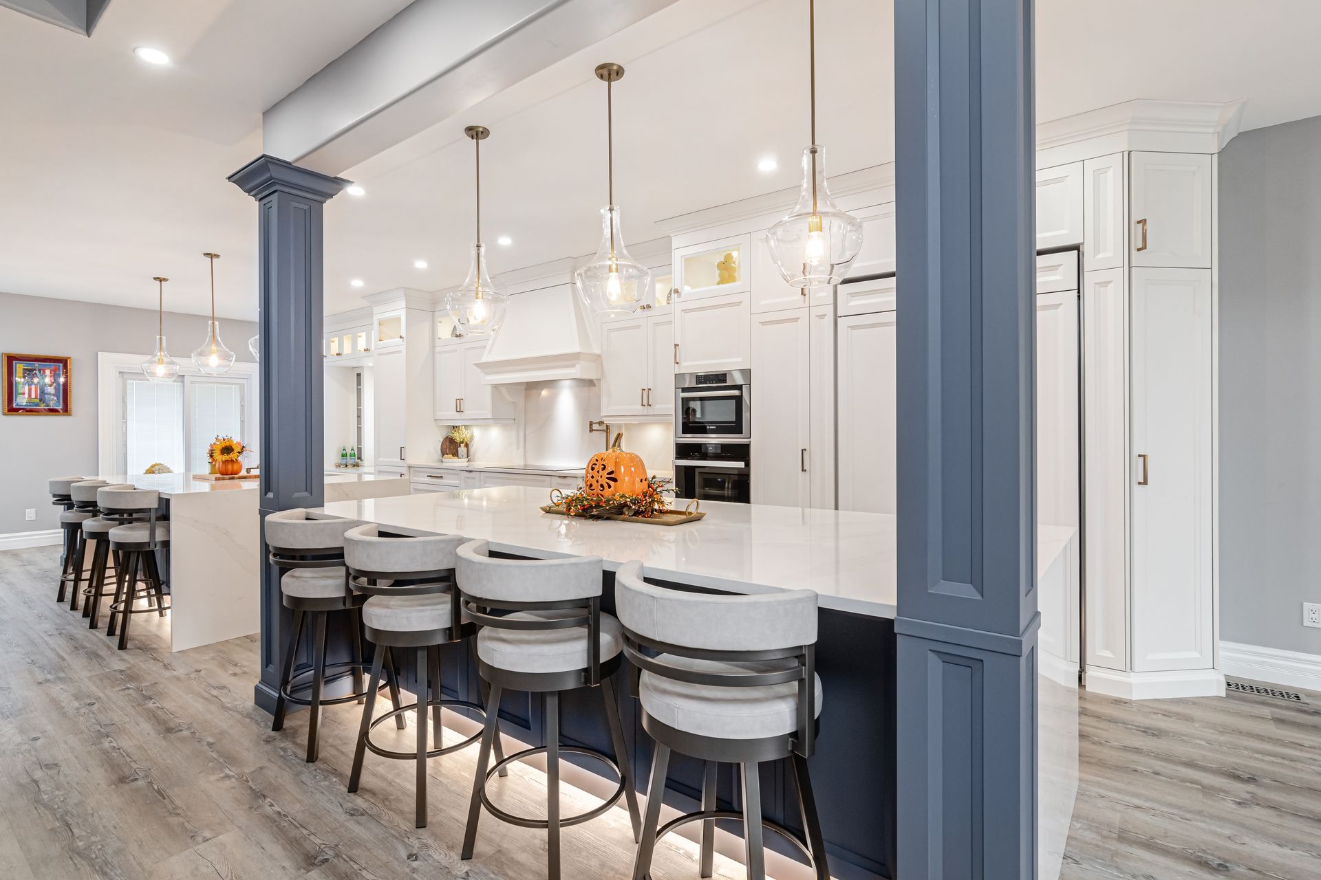 Spacious, bright kitchen with blue island, white cabinets, light wood floor, and pendant lights.