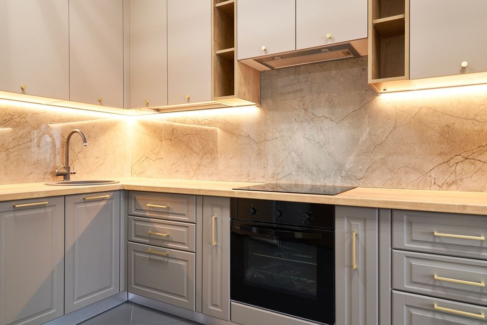 Modern kitchen with gray shaker cabinets, light wood countertops, marble-patterned backsplash, and integrated lighting.