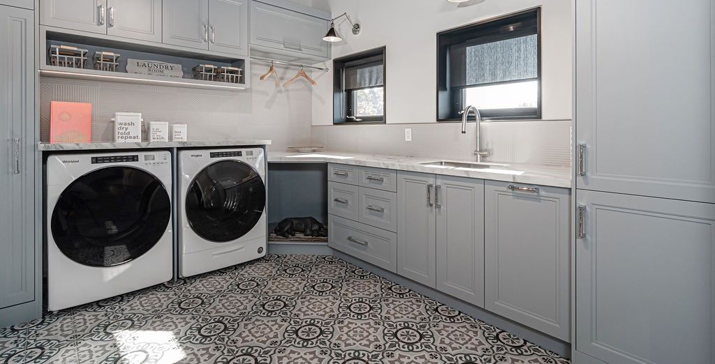 Laundry room with washer, dryer, sink, and patterned floor. Grey cabinets and appliances.