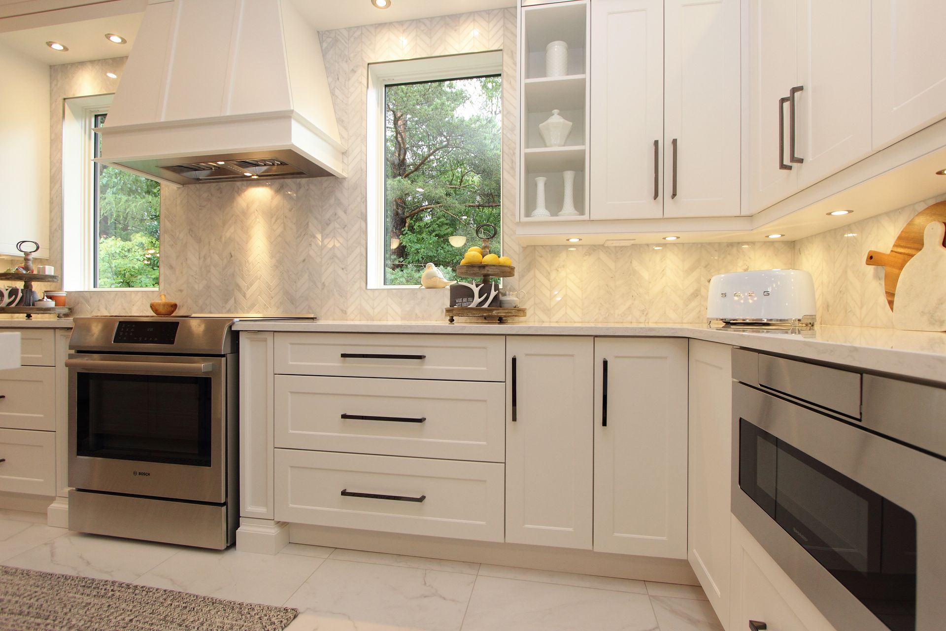 White kitchen with stainless steel appliances, marble backsplash, and under-cabinet lighting.
