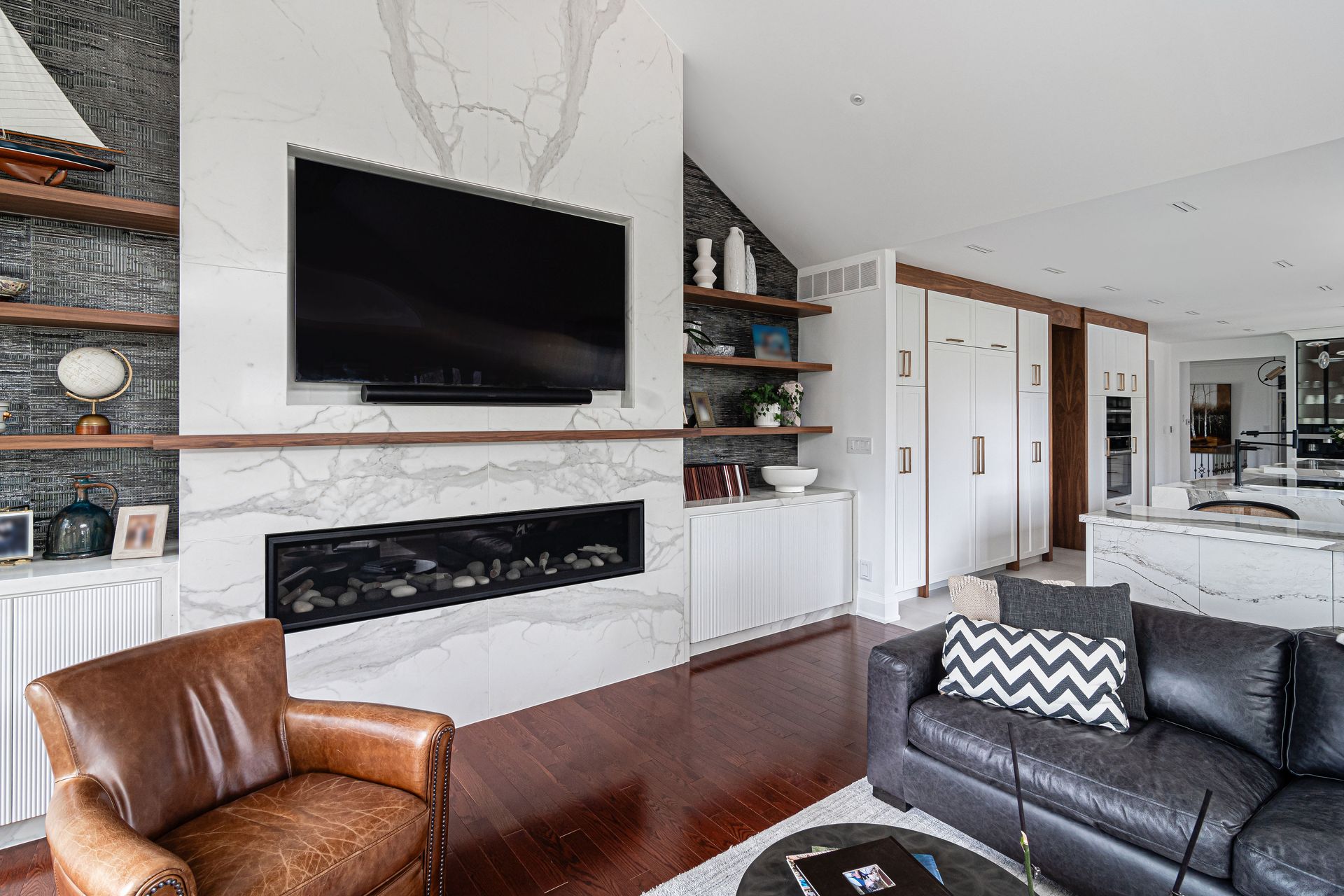 Living room with fireplace, TV, shelves, leather chairs, and dark wood floors.