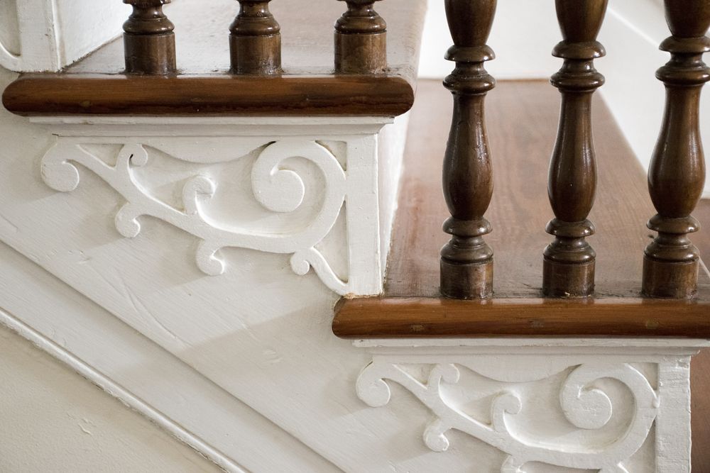 Close-up of staircase side panels featuring intricate white scrollwork carvings beneath wooden steps and brown balusters.