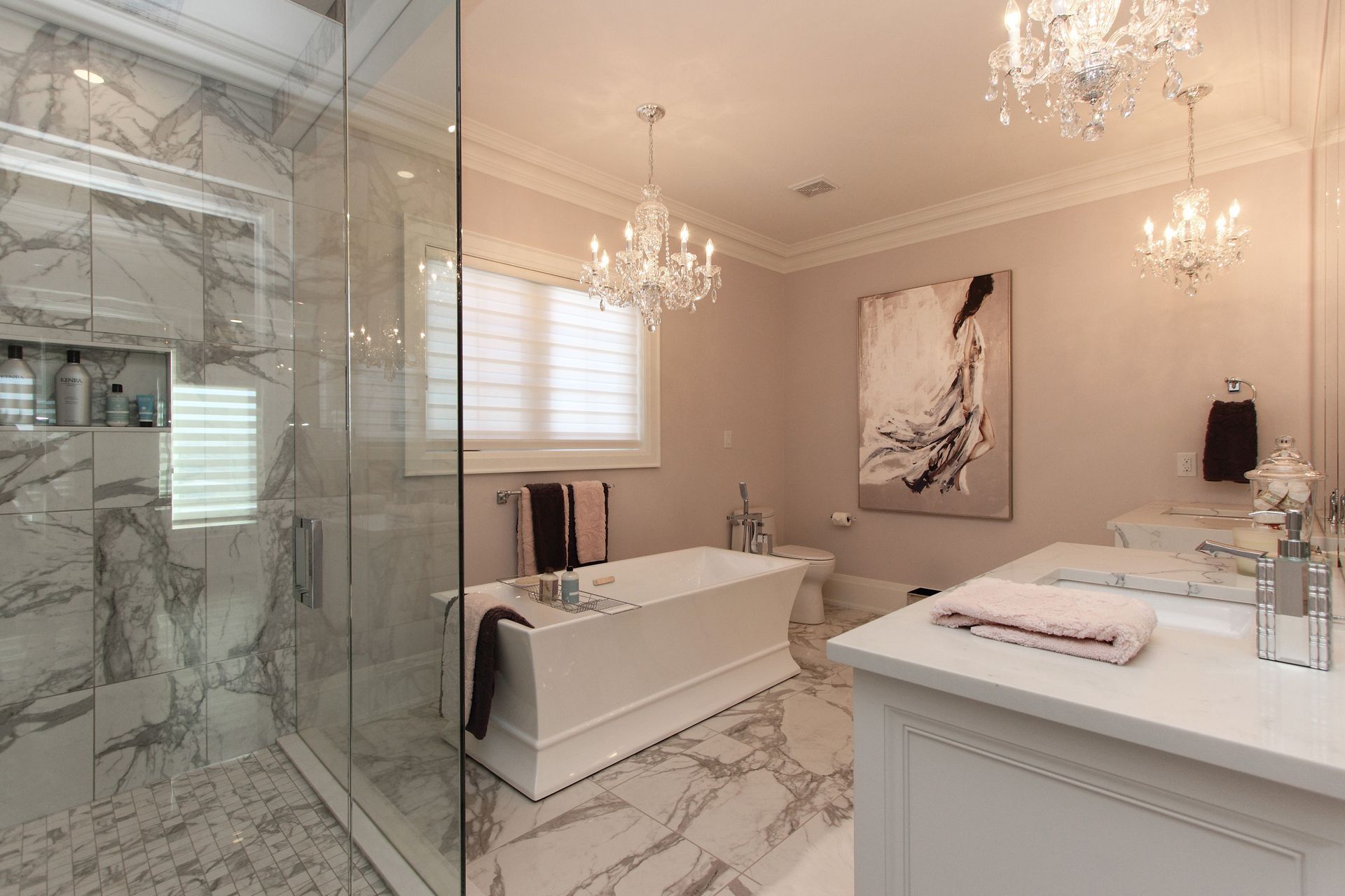 Luxurious bathroom with marble shower, freestanding tub, chandeliers, and artwork.