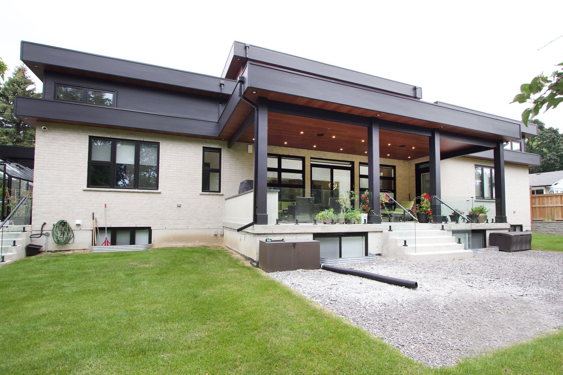 Modern home exterior with a covered porch and green lawn. Light brick walls, black roof, and large windows.