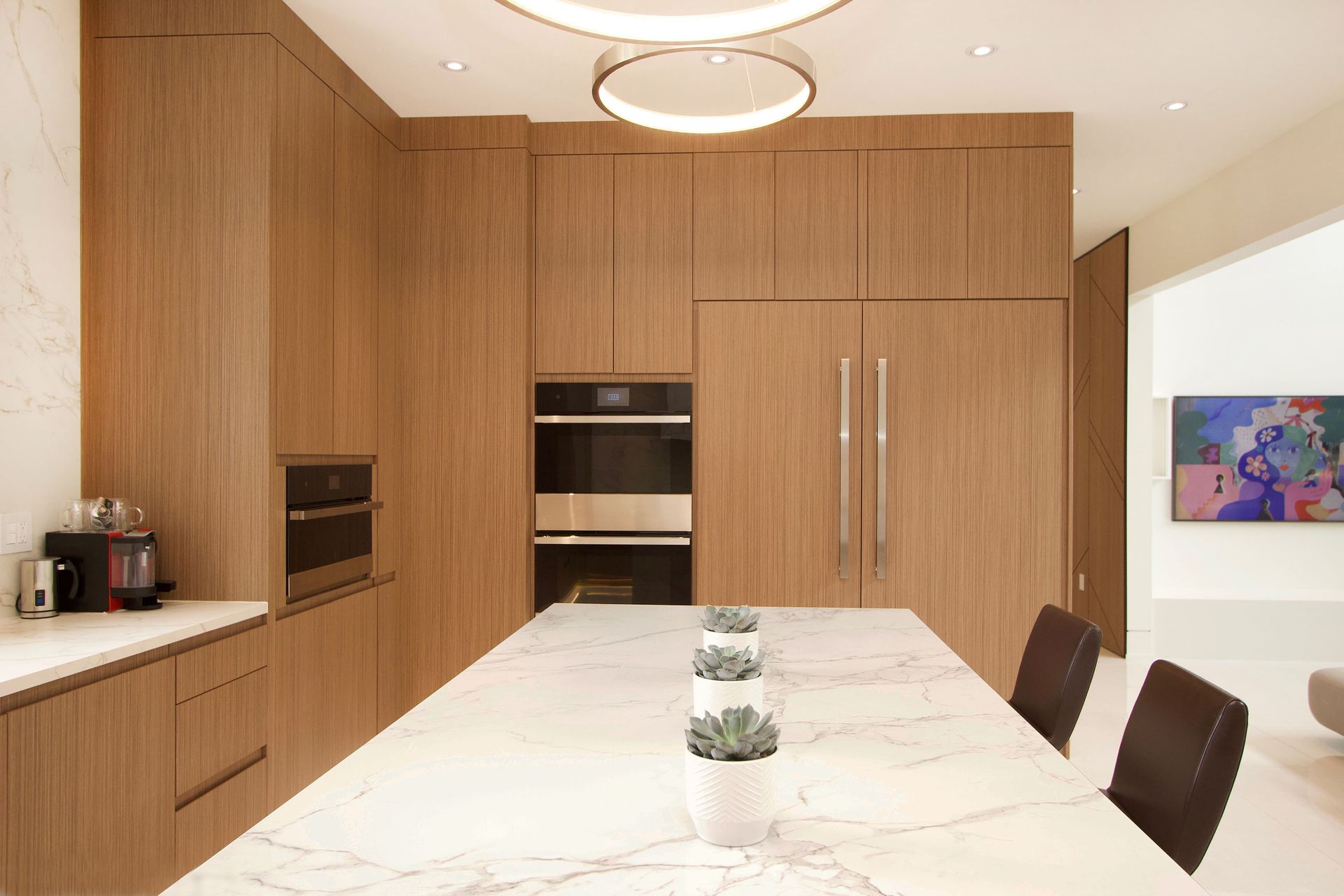 Modern kitchen with light wood cabinetry, white marble island, and recessed lighting.
