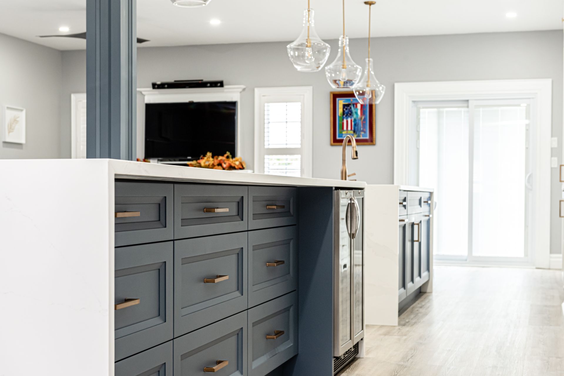 Blue kitchen island with drawers and a wine fridge, gray walls, overhead lights.