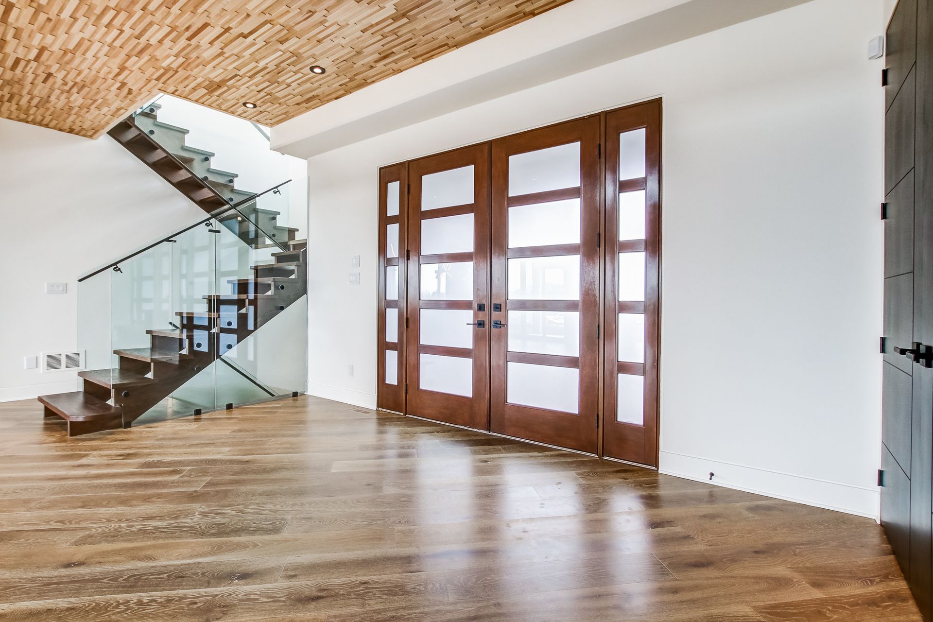 Empty foyer with wood flooring, staircase with glass railing, and double doors with frosted glass.