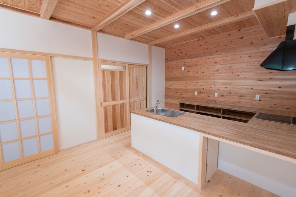 Modern kitchen with light wood flooring, horizontal wood-paneled walls, and a white island counter with a sink.