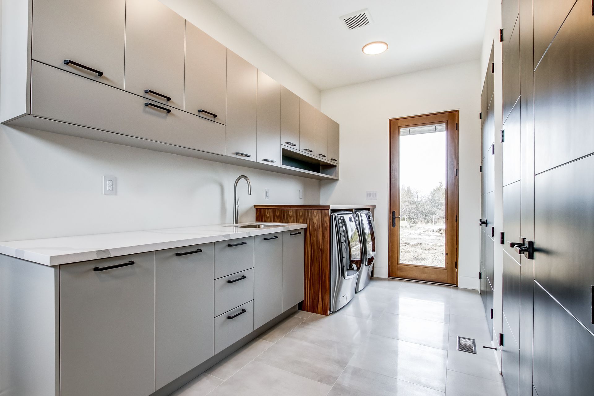 Modern laundry room with gray cabinets, white countertop, and wood door.