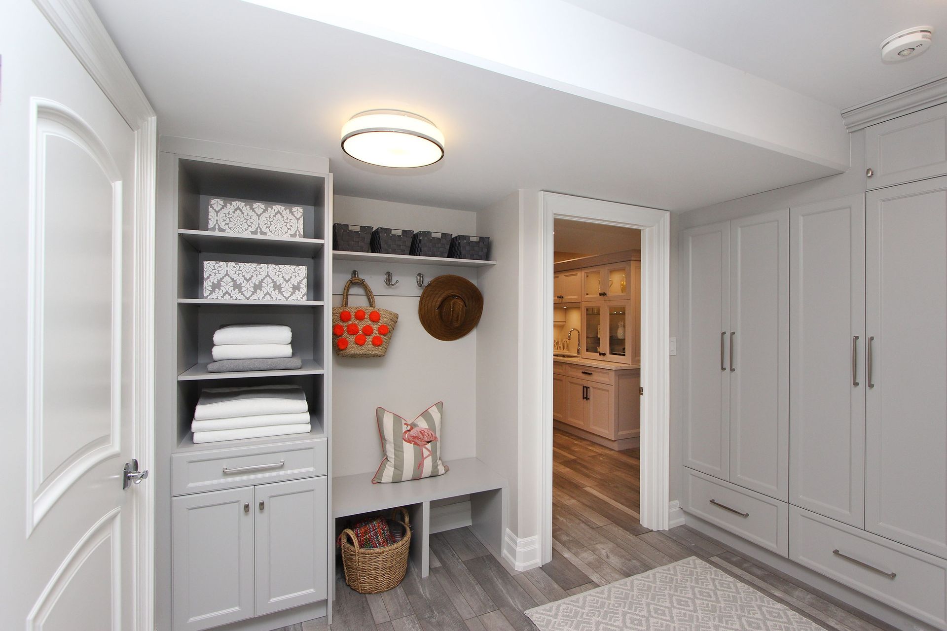 Gray-toned mudroom with built-in storage, bench, and doorway leading to a brightly lit room.