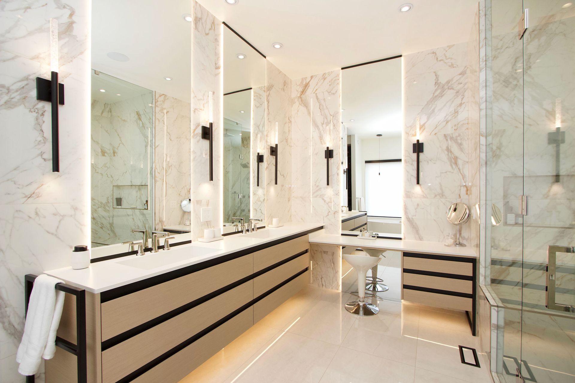 Luxurious bathroom with marble walls, large mirrors, long vanity, and black accents.