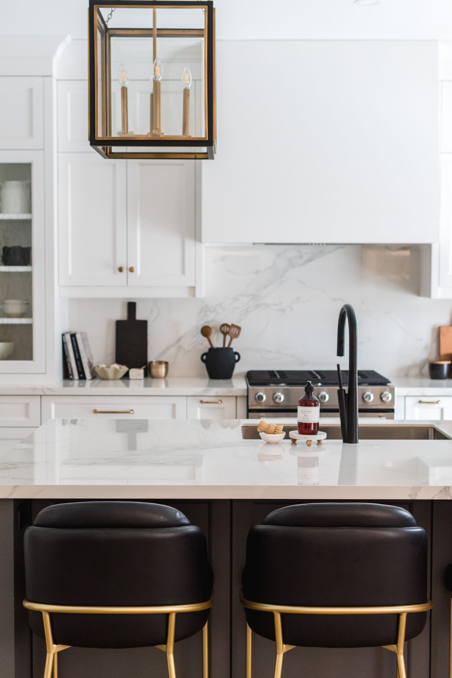 A kitchen with white cabinets , black chairs , a sink and a stove.