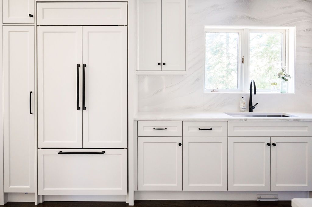 A kitchen with white cabinets , a sink , and a refrigerator.
