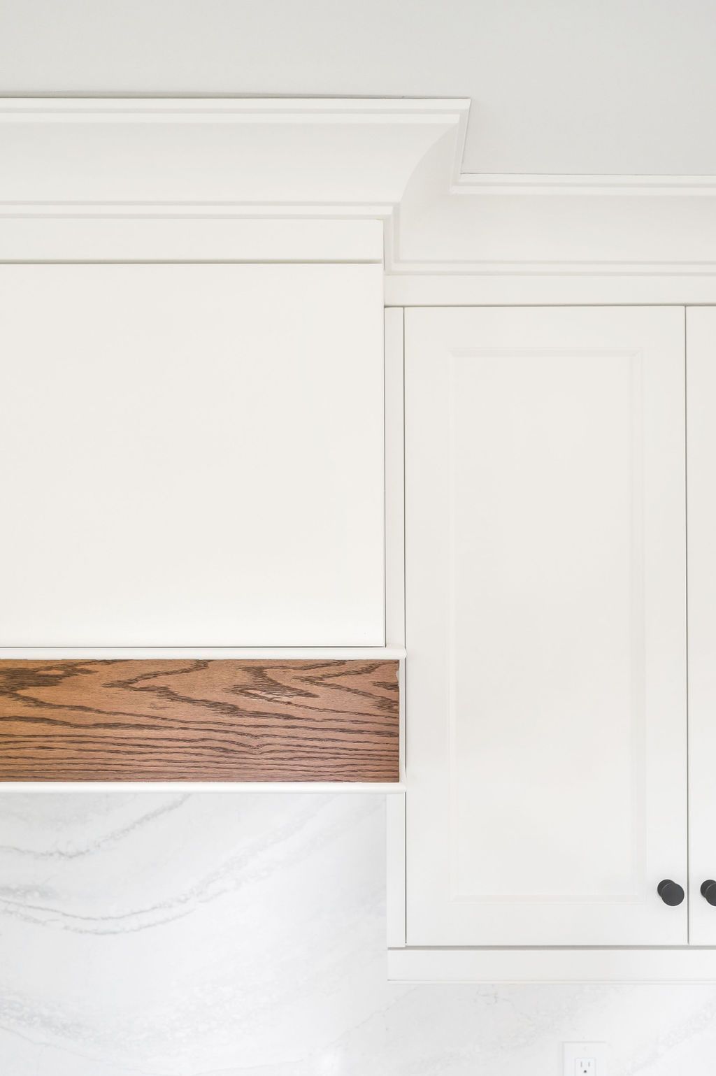 A kitchen with white cabinets and a wooden hood.