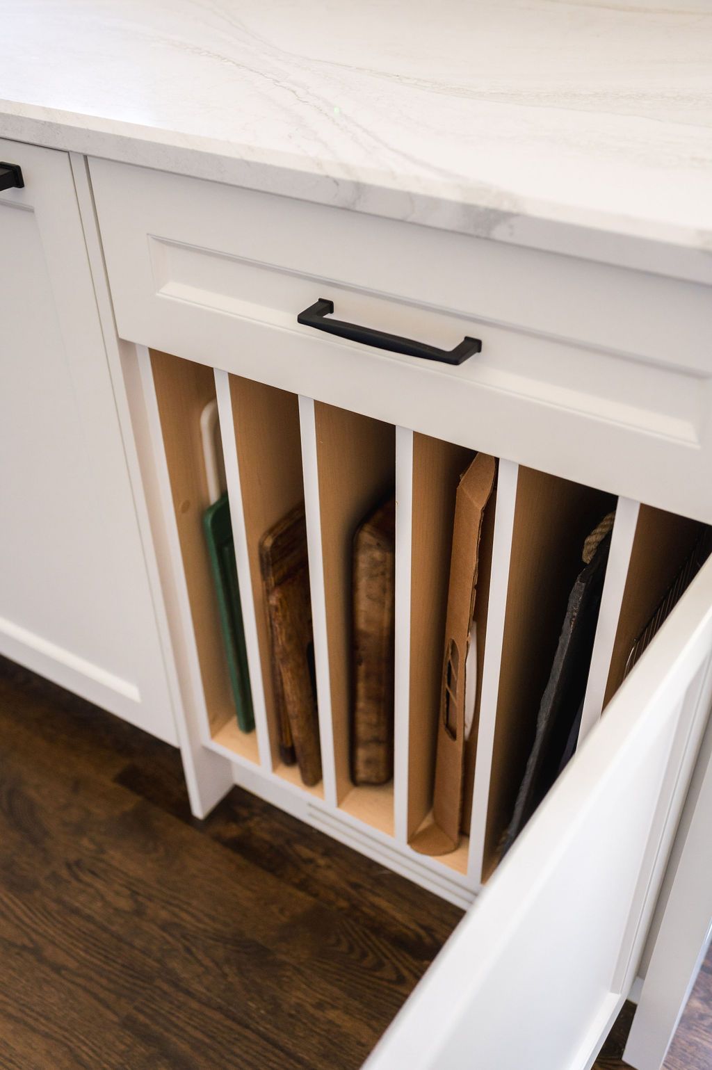 A kitchen cabinet with a drawer filled with cutting boards.