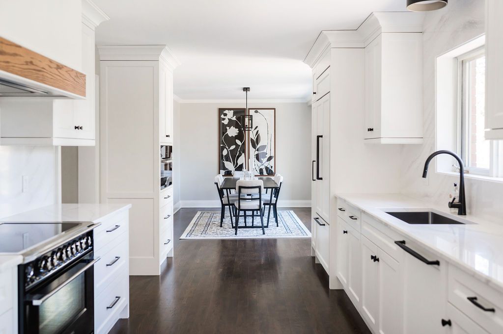 A kitchen with white cabinets , a stove , a sink , and a dining room in the background.