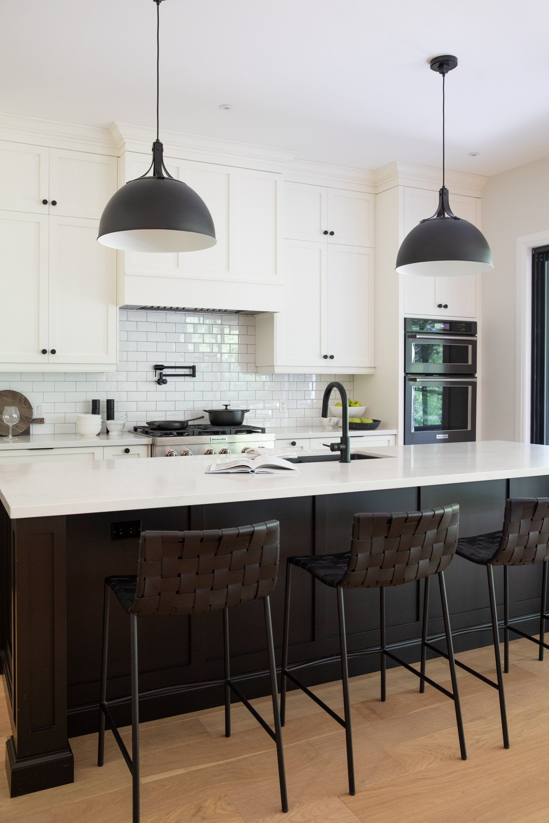 A kitchen with white cabinets , black counter tops , and black stools.
