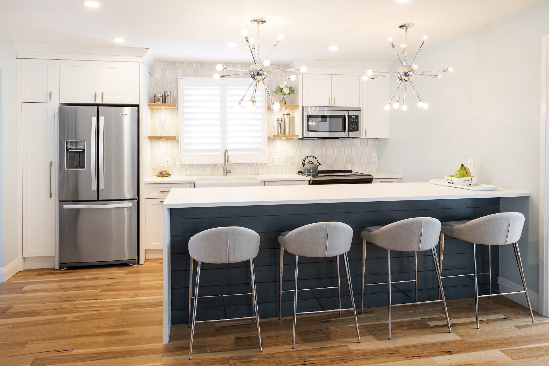 A kitchen with a large island , stools , a refrigerator and a microwave.