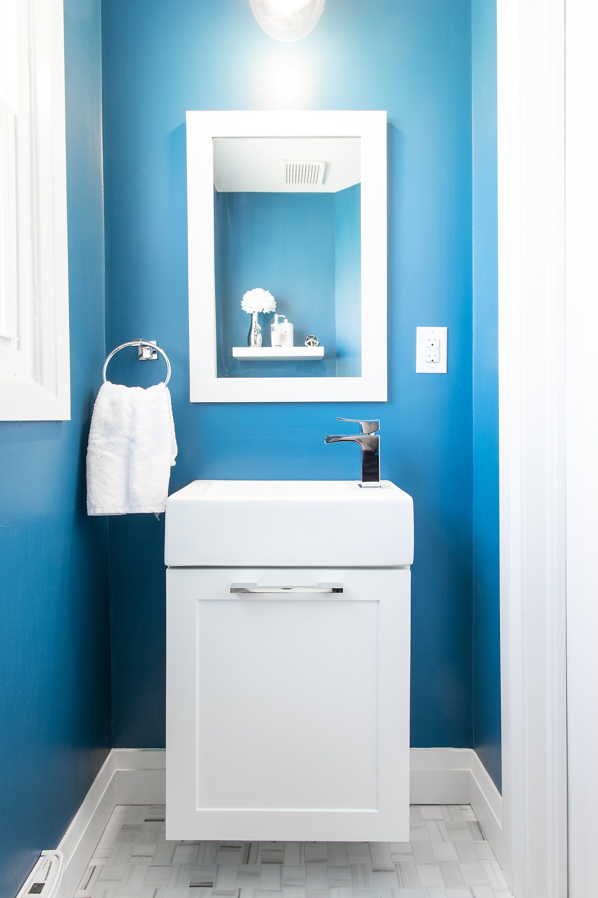 A bathroom with blue walls and a white sink and mirror.