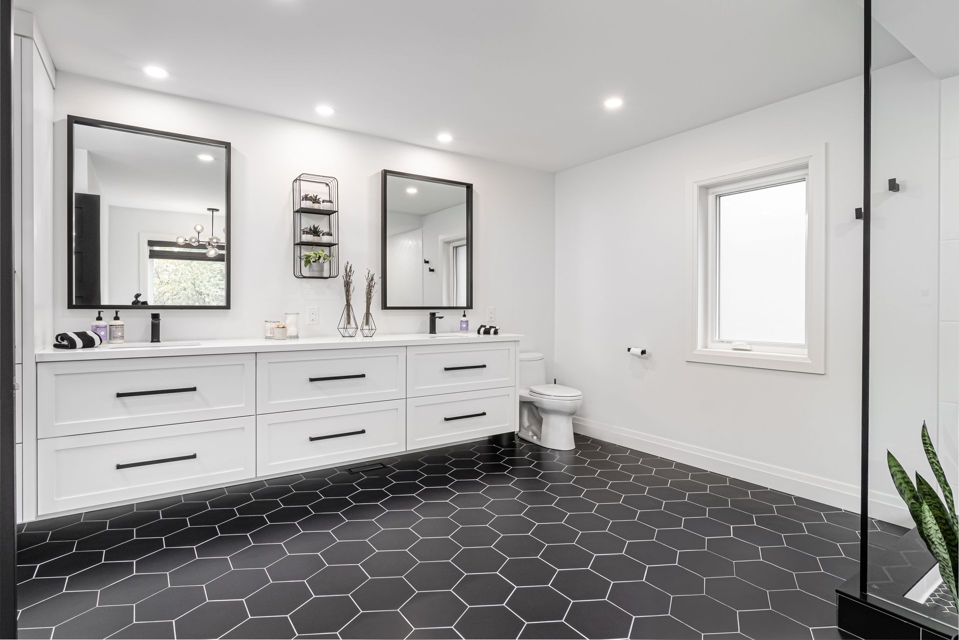A bathroom with two sinks , two mirrors , a toilet and a window.
