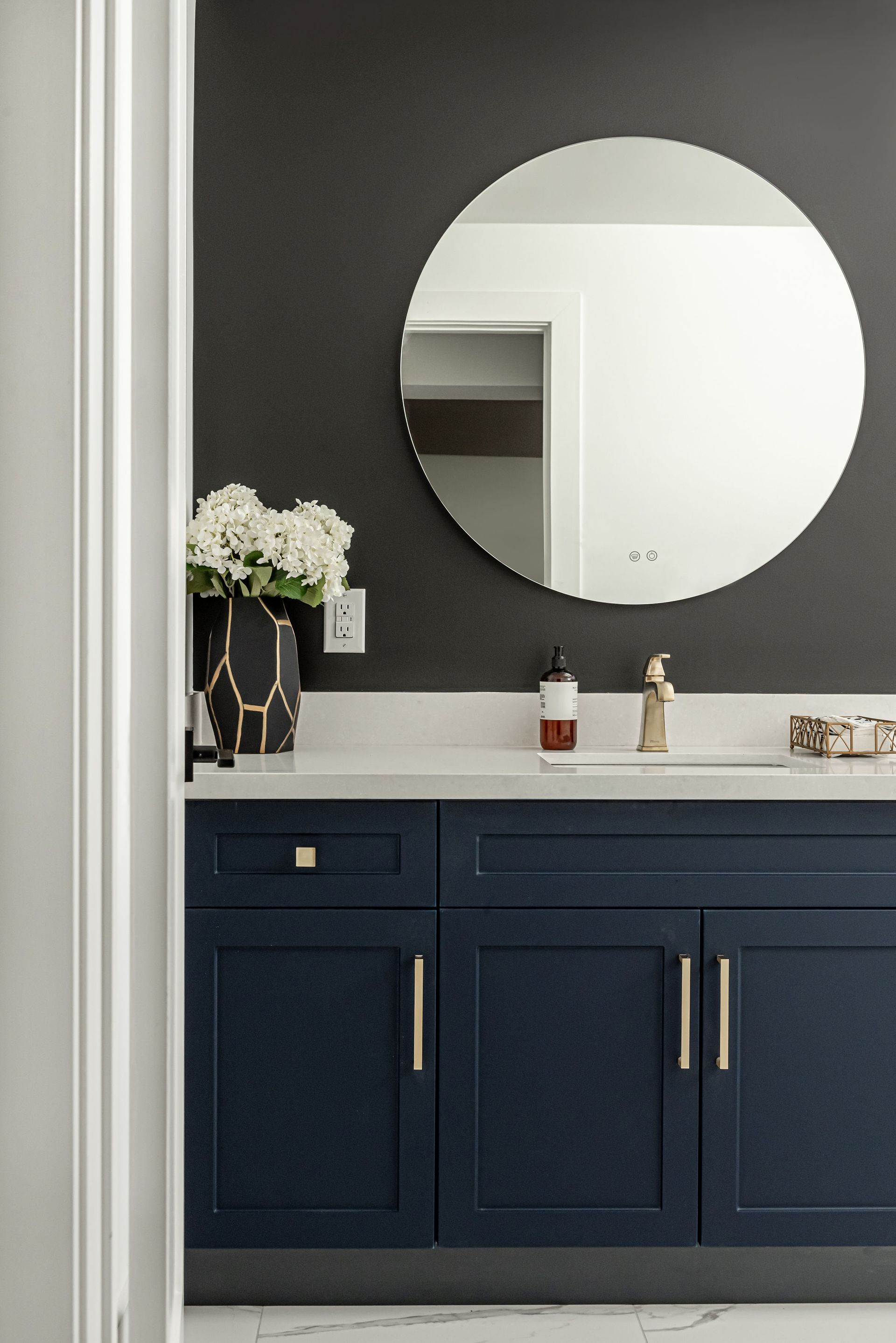 A bathroom with blue cabinets , a round mirror , and a sink.