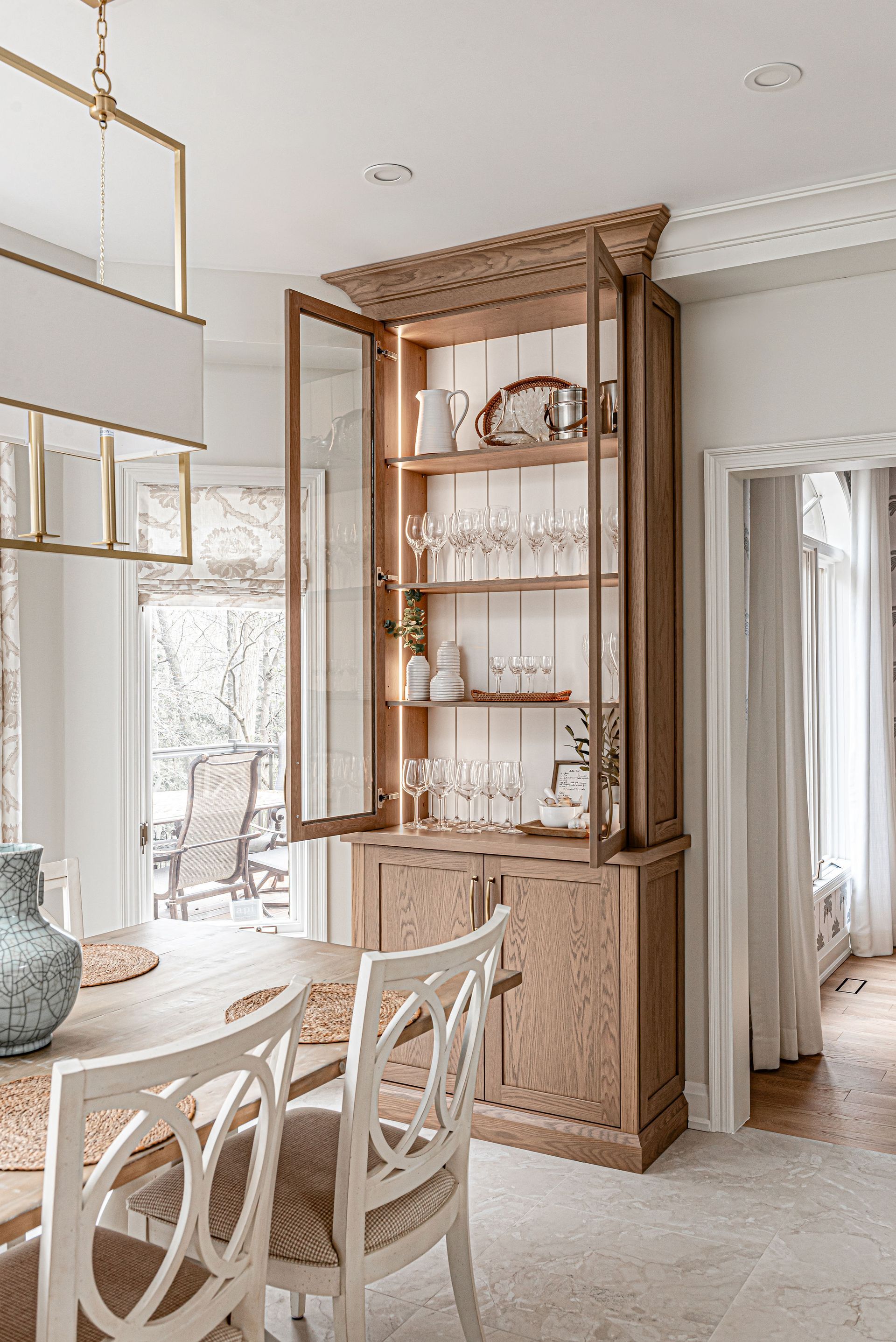 A dining room with a table and chairs and a hutch with the doors open.