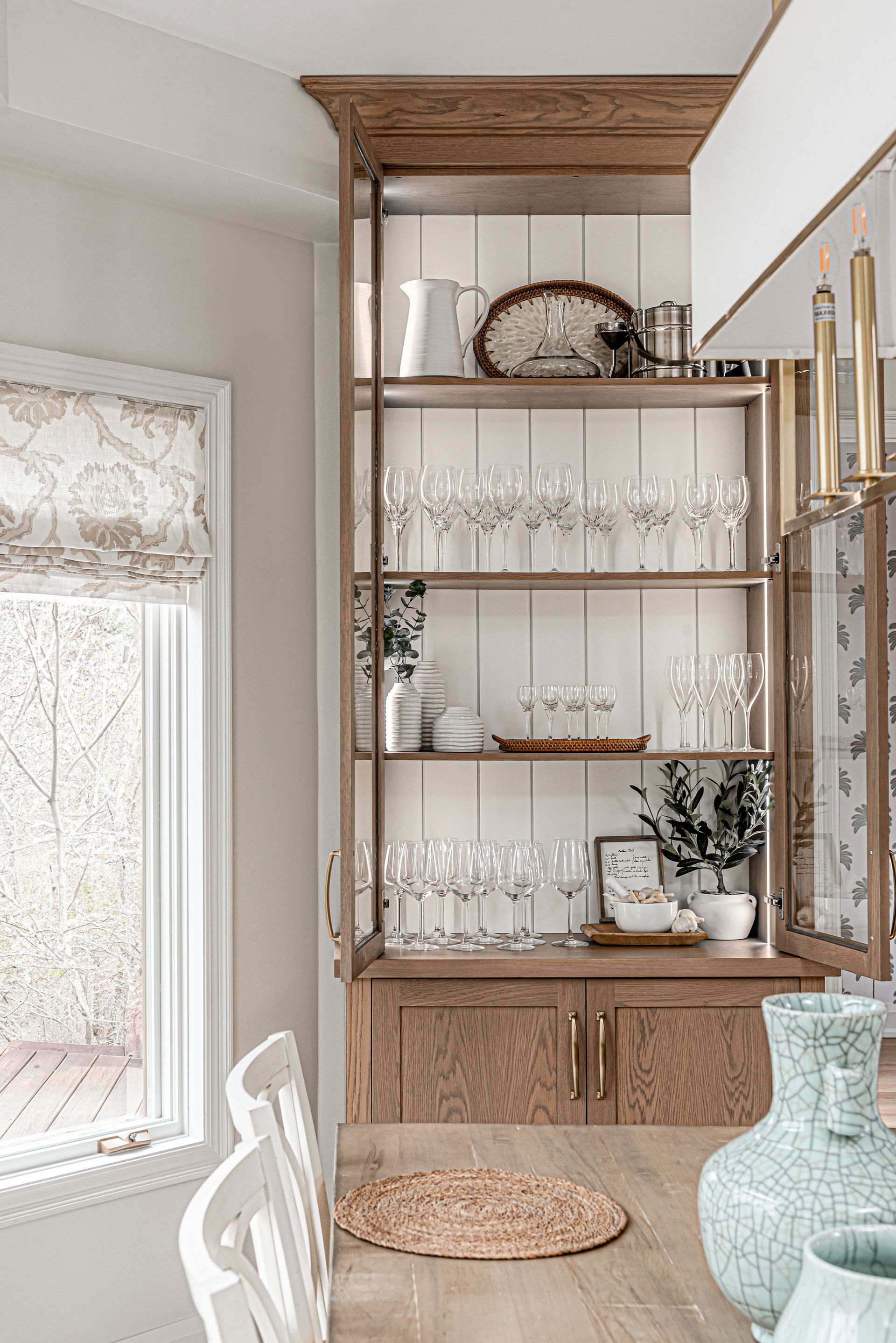 A dining room with a table , chairs , shelves and a window.