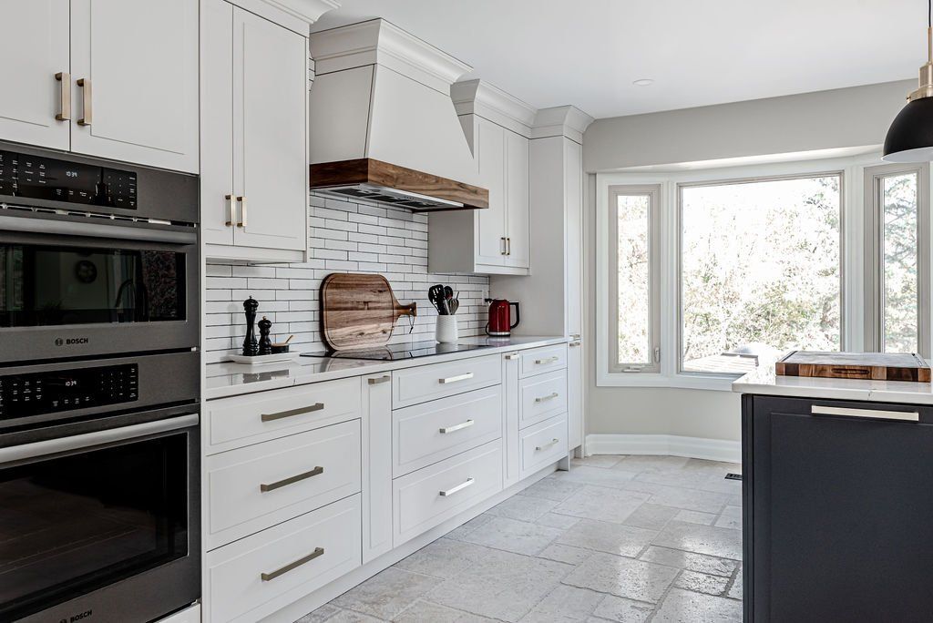 A kitchen with white cabinets , stainless steel appliances , and a large window.