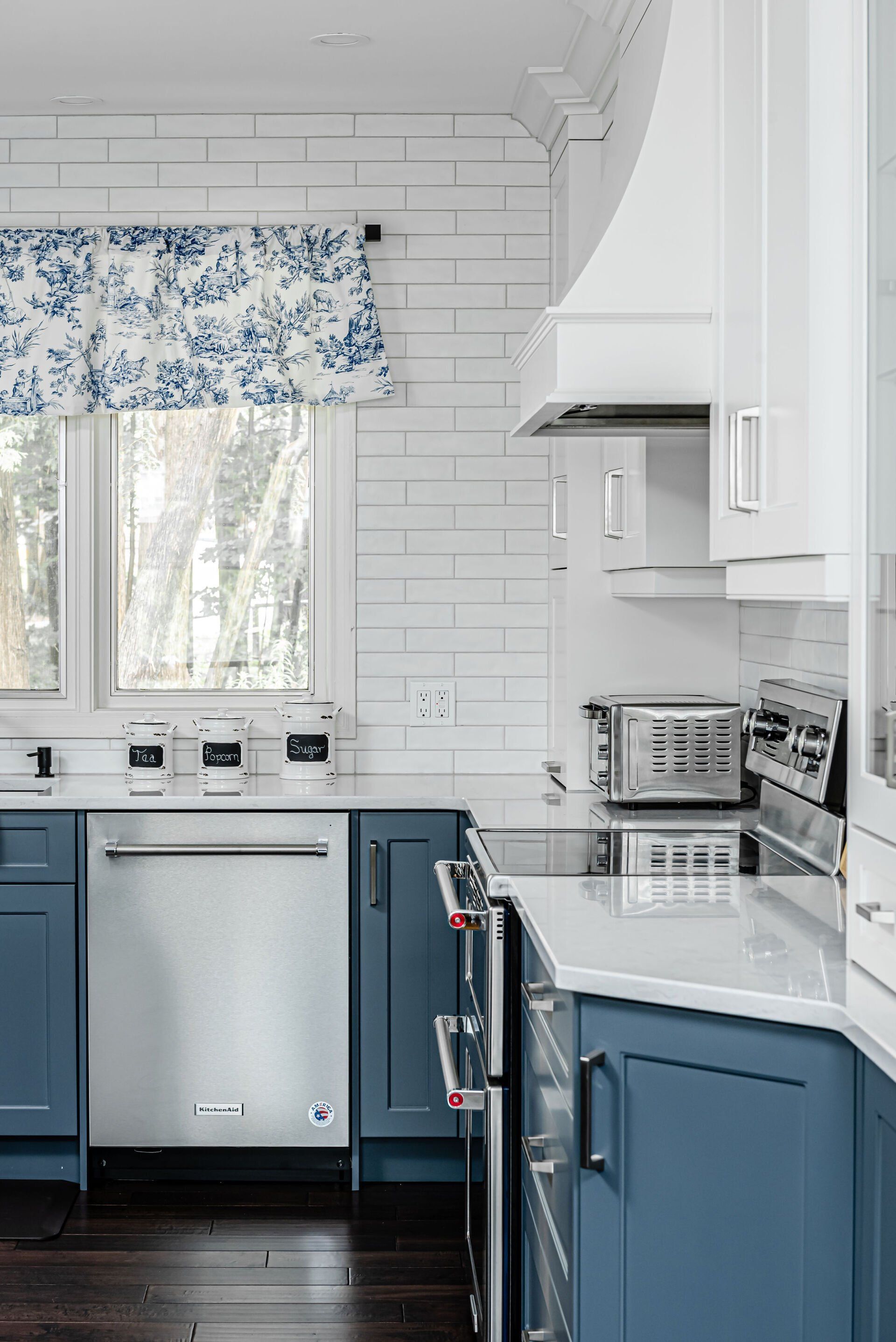 A kitchen with blue cabinets , white cabinets , stainless steel appliances and a window.
