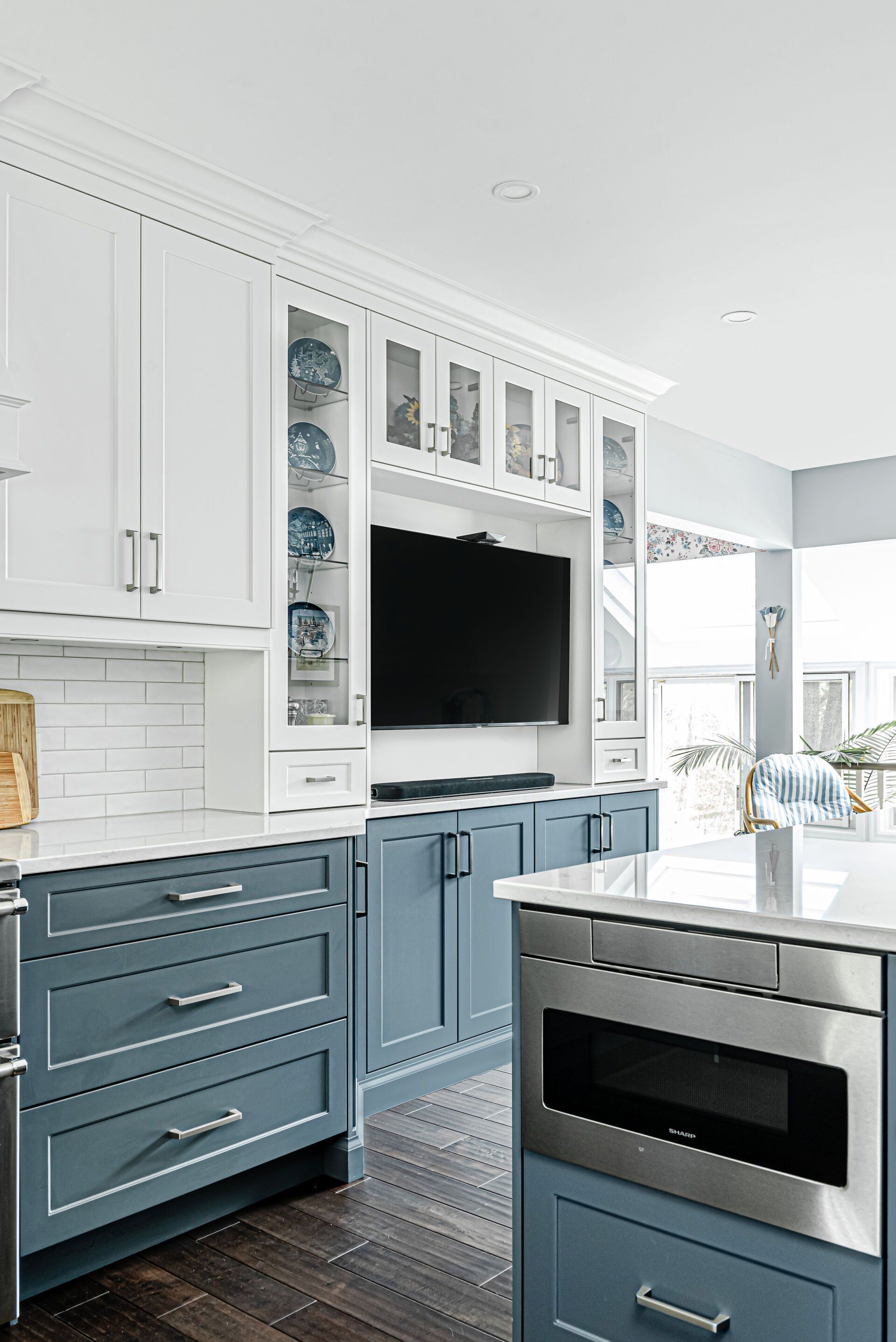 A kitchen with blue cabinets , white cabinets , stainless steel appliances and a flat screen tv.