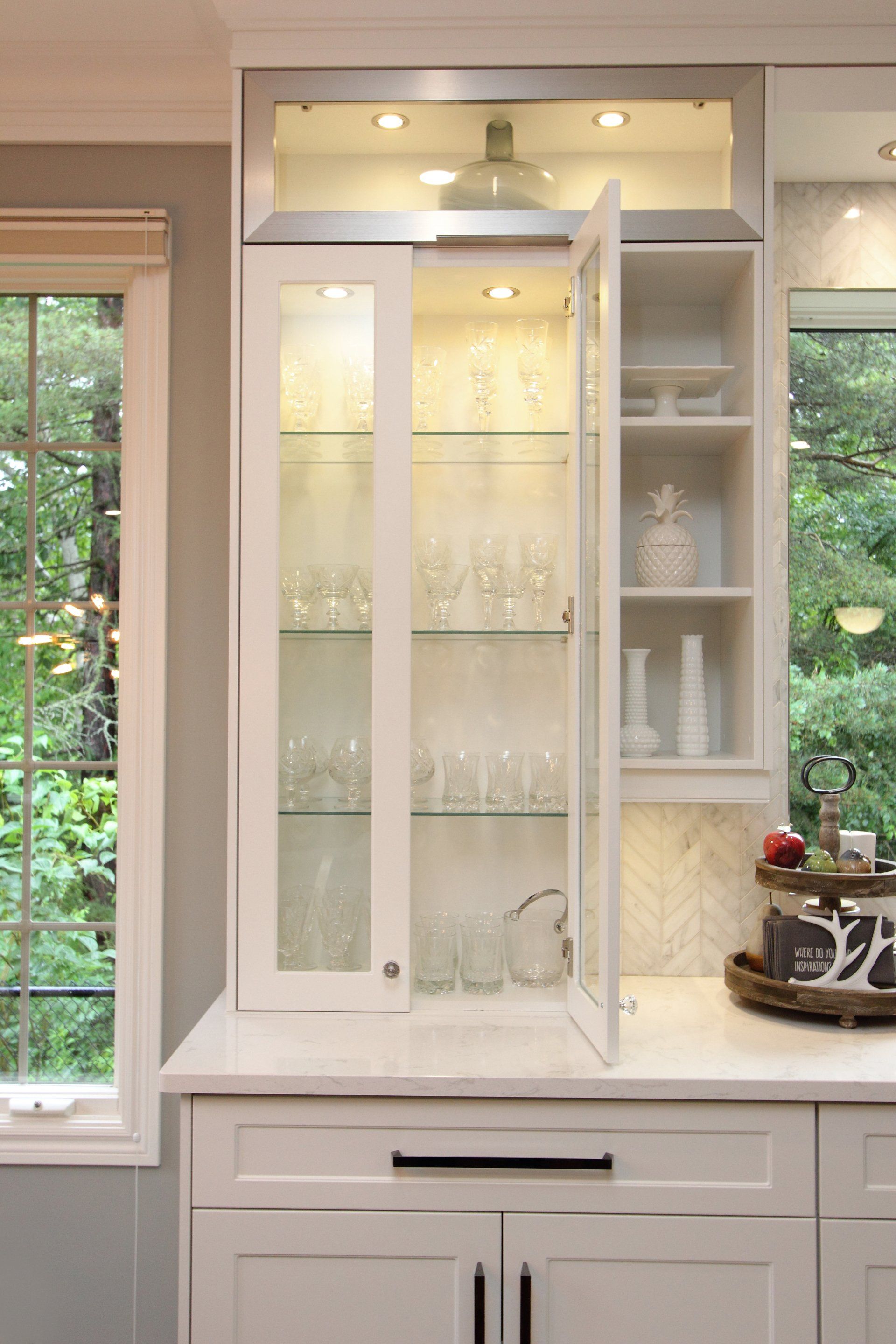 A kitchen with white cabinets and a glass display case.