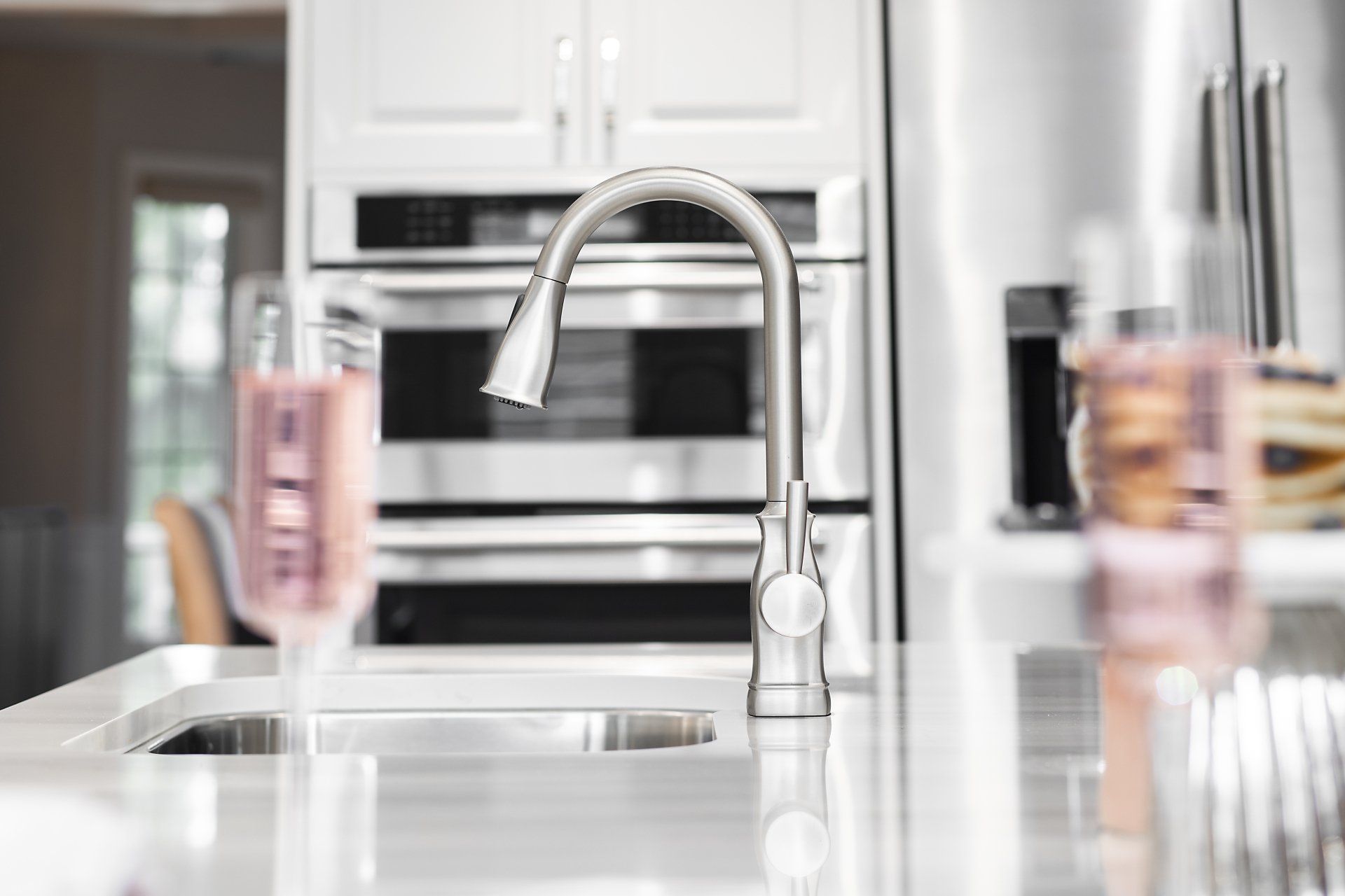 A kitchen sink with a faucet and a glass of wine on the counter.