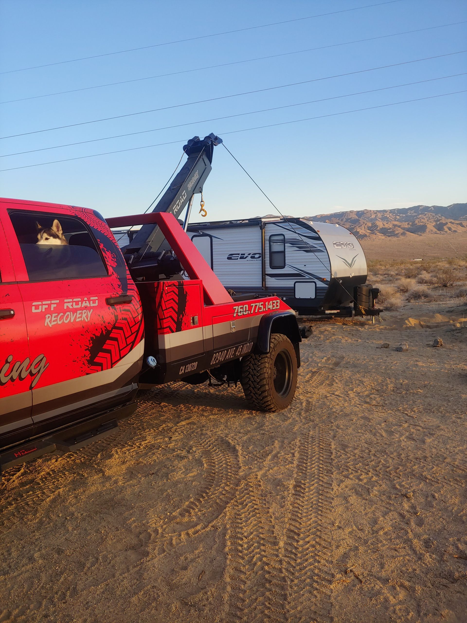 A red tow truck is towing a trailer in the desert.