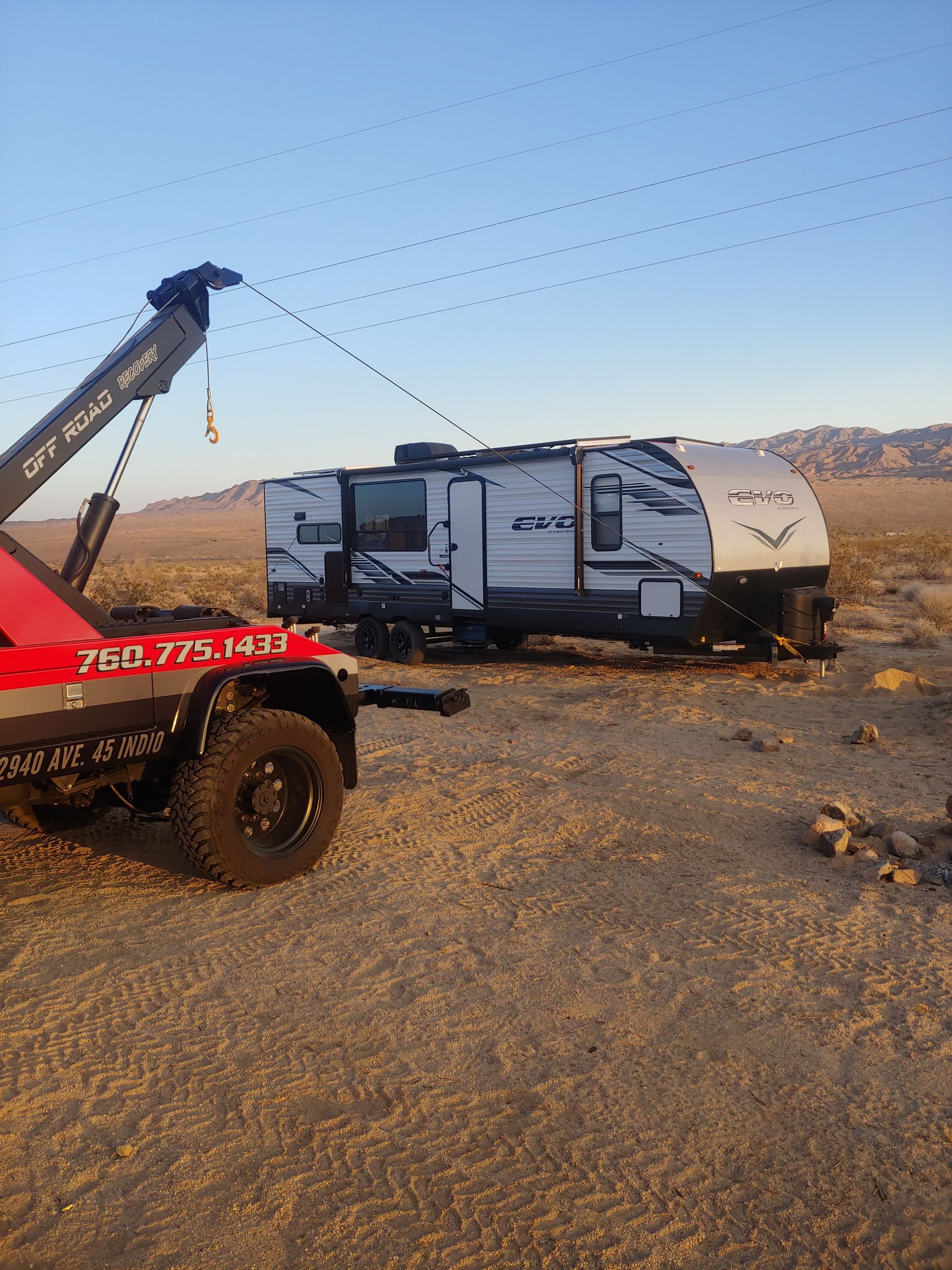A tow truck is towing a camper in the desert.