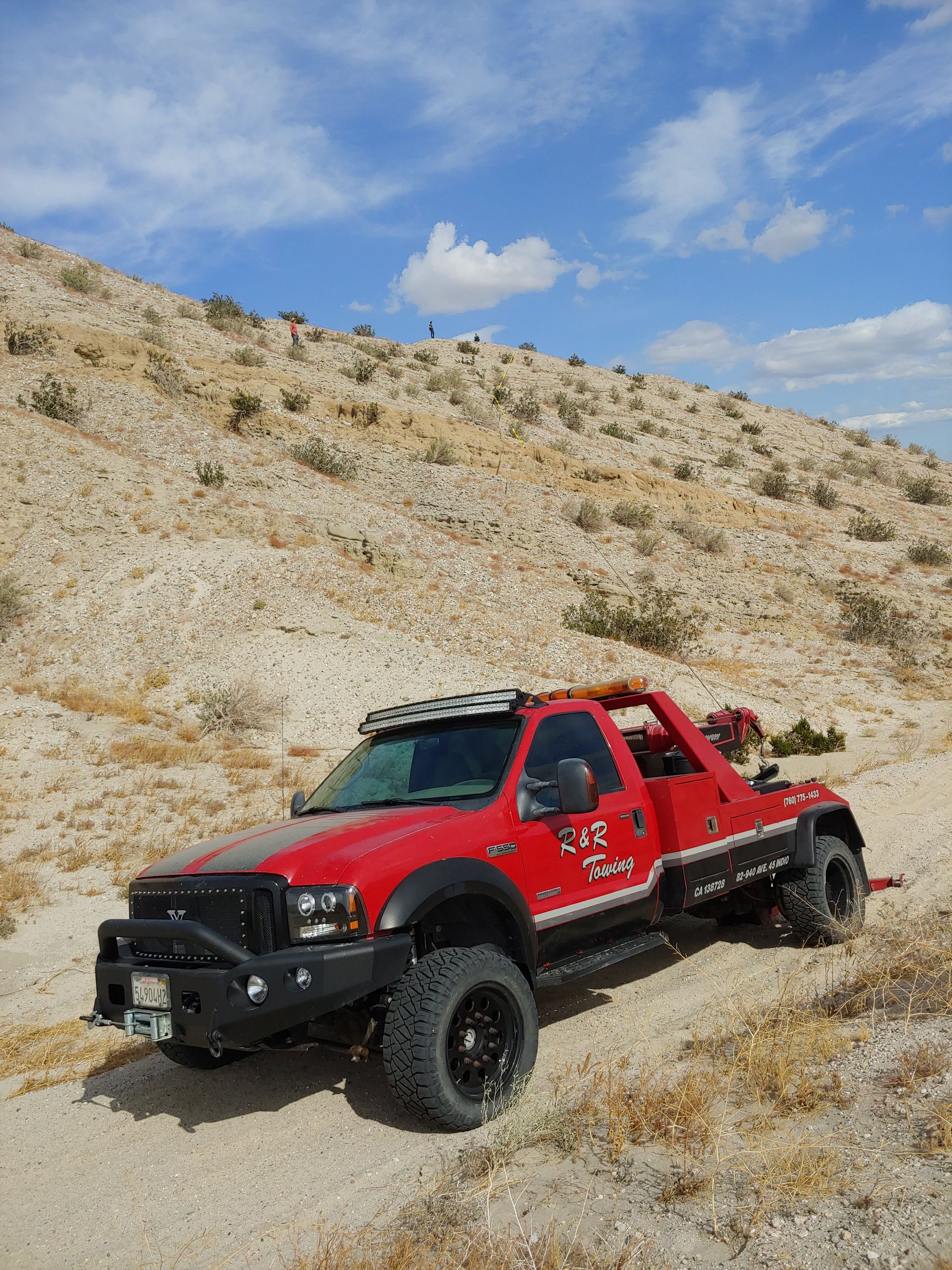 A red tow truck is parked on a dirt road in the desert